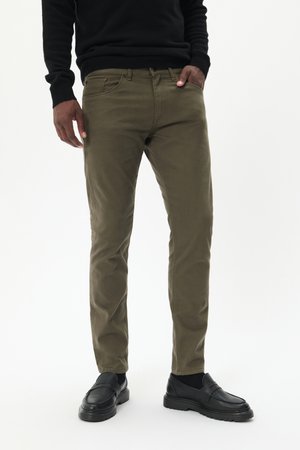 Pantalones ajustados de color verde oliva, hechos de algodón, que cuentan con un bolsillo en la cintura y cinturillas clásicas, combinados con zapatos negros de tipo slip-on.