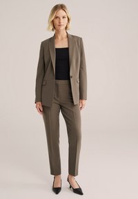 Khaki blazer se sladěnými kalhotami na míru; hladká tkanina; zapínání na jeden knoflík; slim fit; kombinováno s černým topem a černými podpatky.