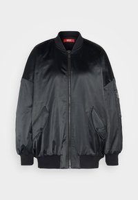 Blouson aviateur en satin noir avec fermeture éclair à l'avant, col et poignets côtelés, et deux poches latérales. Comprend une poche zippée sur la manche gauche.