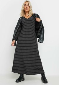 Grårandig maxiklänning med långa ärmar och V-ringning, kombinerad med en svart läderjacka och svarta snörkängor. Slät textur.