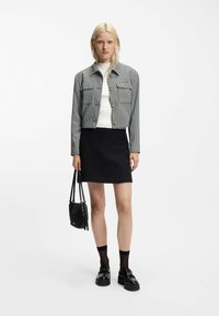 Giacca corta grigia a quadri con bottoni dorati, maglione bianco a coste, gonna nera texturizzata, borsa nera e scarpe nere robuste.