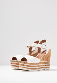 Sandali platform bianchi con design in sughero, punta aperta, cinturino alla caviglia regolabile e tomaia texturizzata con dettagli decorativi.
