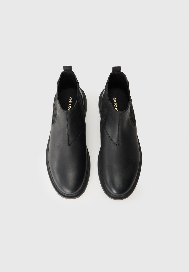 Chaussures en cuir noir à enfiler avec des panneaux élastiques sur les côtés, bout rond, texture lisse, design minimaliste, avec une languette au talon.