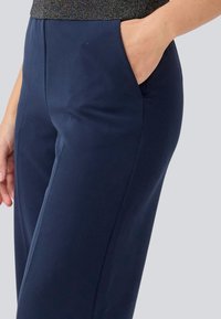 Navy blue trousers with a relaxed fit, featuring a side pocket and smooth texture. The waistband is slightly tailored for a secure fit.