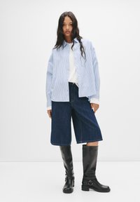 Lyseblå stribet oversized skjorte, hvid t-shirt, mørk denim culottes og knæhøje sorte støvler med spænder. Simpelt, casual design.