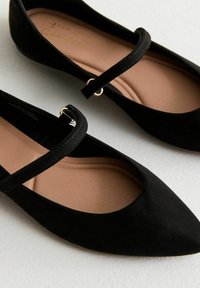 Svarta mocka balletlägenheter med spetsig tå, prydda med ett dekorativt band och detaljer i guldton. Ljusbeige innersula för komfort.
