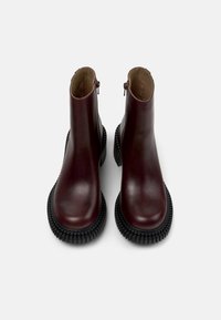 Botines burdeos con acabado de piel lisa, suela de goma antideslizante y cremalleras laterales para facilitar el calce. Líneas limpias y un diseño moderno.