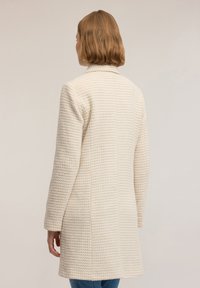 Beżowy płaszcz o fakturze z dopasowanym krojem, z długimi rękawami i średnią długością. Gładka tkanina i minimalistyczny styl.