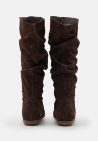 Bottes en daim marron hauteur genou avec un design décontracté. Texture douce, bout arrondi et semelle plate. Accentuées par un matériau plié en haut.
