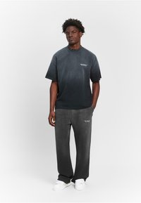 Schwarzes oversized T-Shirt mit "RETERNITY"-Logo, kombiniert mit passenden grauen Jogginghosen. Beide Teile bestehen aus einem weichen, strukturierten Stoff. Weiße Sneaker.