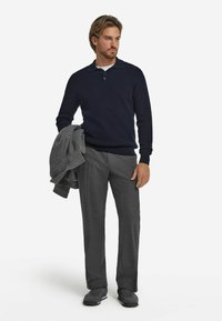 Marinblå ribbad stickad tröja, grå skräddarsydda byxor, håller en grå blazer och grå sneakers. Avslappnad smart design med texturerad stickning.