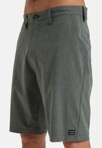 Pantaloni corti verdi in tessuto testurizzato. Presentano una chiusura con bottone, tasche frontali e una piccola etichetta con logo sull'orlo.