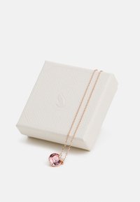Collier en or rose avec une grande pierre précieuse rose dans un cadre circulaire, accompagné d'une chaîne délicate. Emballé dans une boîte blanche texturée.