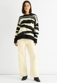 Black and white striped sweater with a loose fit, soft texture, wide sleeves; paired with cream wide-leg trousers and black ankle boots.