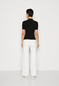 Haut noir à manches courtes avec un col haut, associé à un pantalon large blanc. La tenue a un design simple et contemporain.
