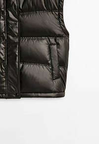 Veste noire matelassée sans manches avec fermeture à boutons-pression et poche latérale verticale sur fond blanc.