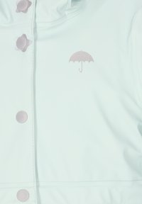 Svetlo modra dežna jakna z gumbi v obliki cvetov, ki ima na sprednji strani majhen rožnat dežnik. Gladek, vodoodporen material.