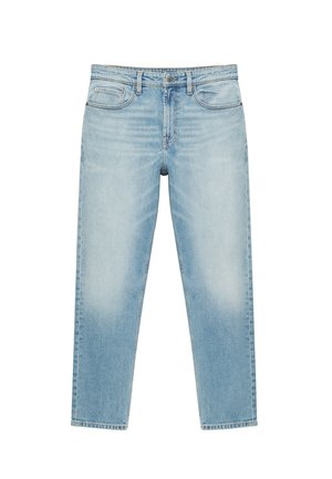 Persona con la pelle scura che indossa una camicia bianca a maniche corte e jeans azzurri, con le braccia incrociate sul petto.