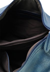 De binnenkant van de blauwe leren tas met een donkere voering, voorzien van een ritsvak en een gladde textuur. Geopend uitzicht dat de indeling van de compartimenten toont.