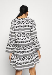 Robe à motifs noir et blanc avec manches longues évasées, présentant des dessins géométriques et un ourlet évasé. Texture de tissu lisse.