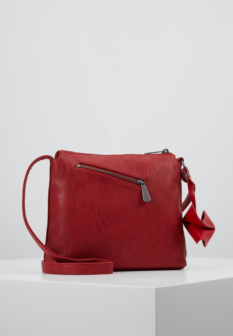 Sac bandoulière en cuir rouge avec une poche zippée diagonale à l'avant et une sangle réglable, posé sur une surface blanche.
