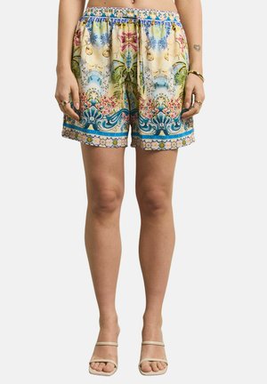 Woman wearing colorful patterned shorts with floral and blue decorative designs, cream heeled sandals, rings, and a gold bracelet.
