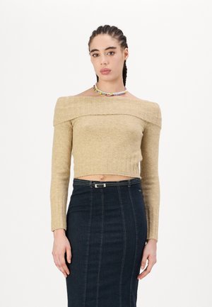 Beige cropped sweater with off-the-shoulder design, ribbed texture, and long sleeves. Paired with a dark denim pencil skirt featuring stitch lines.