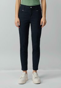 Pantalons slim en bleu marine en tissu mélangé coton, avec une taille mi-haute, cinq poches et de subtils détails de couture. Portés avec des baskets blanches.