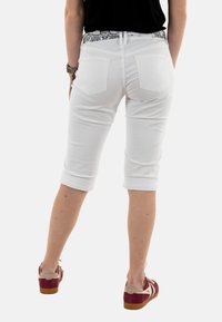 Witte capri-broek met een opgerolde zoom, achterzakken met stikselaccenten en een zwart-wit geblokte tailleband.
