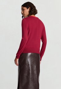Roter, figurbetonter Pullover mit langen Ärmeln, gerippten Bündchen und rundem Ausschnitt, kombiniert mit einem hochtaillierten, glänzenden braunen Lederrock.