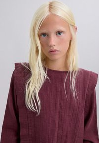 Prenda texturada de color marrón con rayas verticales, que presenta un diseño único en los hombros, escote redondo y tejido suave y fluido.