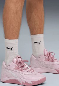 Scarpe sportive rosa con un design strutturato e dettagli bianchi, abbinate a calzini bianchi con un logo nero. Le scarpe hanno lacci e una punta arrotondata.