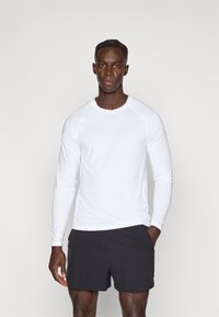 Balts garroku sporta krekls no viegla auduma, ar gludu faktūru un apaļu kakla izgriezumu, kopā ar melniem šortiem.