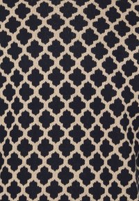 Tessuto lavorato a maglia caratterizzato da un motivo geometrico di forme blu navy su sfondo crema, con dettagli testurizzati in tutta la superficie.