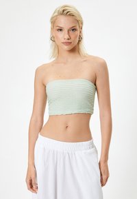 Jasnozielony, strapless crop top o teksturowanym, plisowanym wzorze. W połączeniu z białymi, luźnymi szortami. Styl minimalistyczny, bez widocznych wzorów.