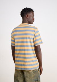 Camiseta de algodón a rayas amarillas y azules con mangas cortas y cuello redondo, mostrada desde la espalda, revelando el patrón de rayas y el ajuste.