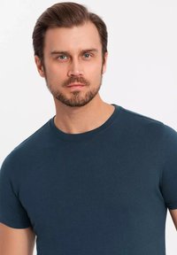 Ciemnoniebieska dopasowana koszulka z okrągłym dekoltem, krótkimi rękawami i gładkim, teksturowanym materiałem. Prosty wzór bez widocznych nadruków czy akcentów.