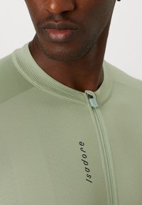 Mintgrünes Radtrikot mit einem Reißverschluss vorne, geripptem Kragen und dezentem Branding. Der Stoff wirkt glatt und hat ein tailliertes Design.