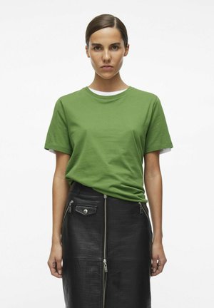 Groene katoen t-shirt gelaagd over een witte top, gecombineerd met een zwarte leren rok met ritsen en een textuurafwerking.