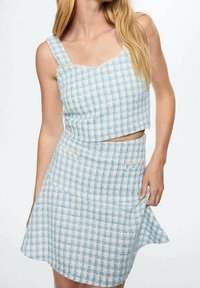 Conjunto de top corto y falda a cuadros en azul y blanco, hecho de una tela texturizada con bordes desflecados. La falda tiene un diseño acampanado y bolsillos.