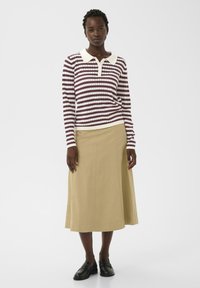 Randig långärmad tröja i burgundy och vitt med krage, kombinerad med en beige knälång kjol och svarta loafers. Släta texturer.