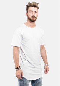 T-shirt en coton blanc avec un col rond, des manches courtes et un ourlet courbé plus long. Associé à un jean bleu déchiré et des bracelets.