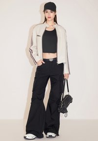 Witte leren bomberjack met bordeauxrode strepen, zwarte crop top, zwarte cargo pants, witte sneakers en een zwart gewatteerde handtas.