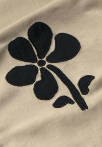 Black flower design on beige fabric, featuring five petals, a central dot, and a stem with leaves, outlined in a contrasting stitch.