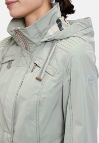 Light grey waterproof jacket with a hood, featuring contrasting inner lining, zippered pockets, and adjustable drawstrings.