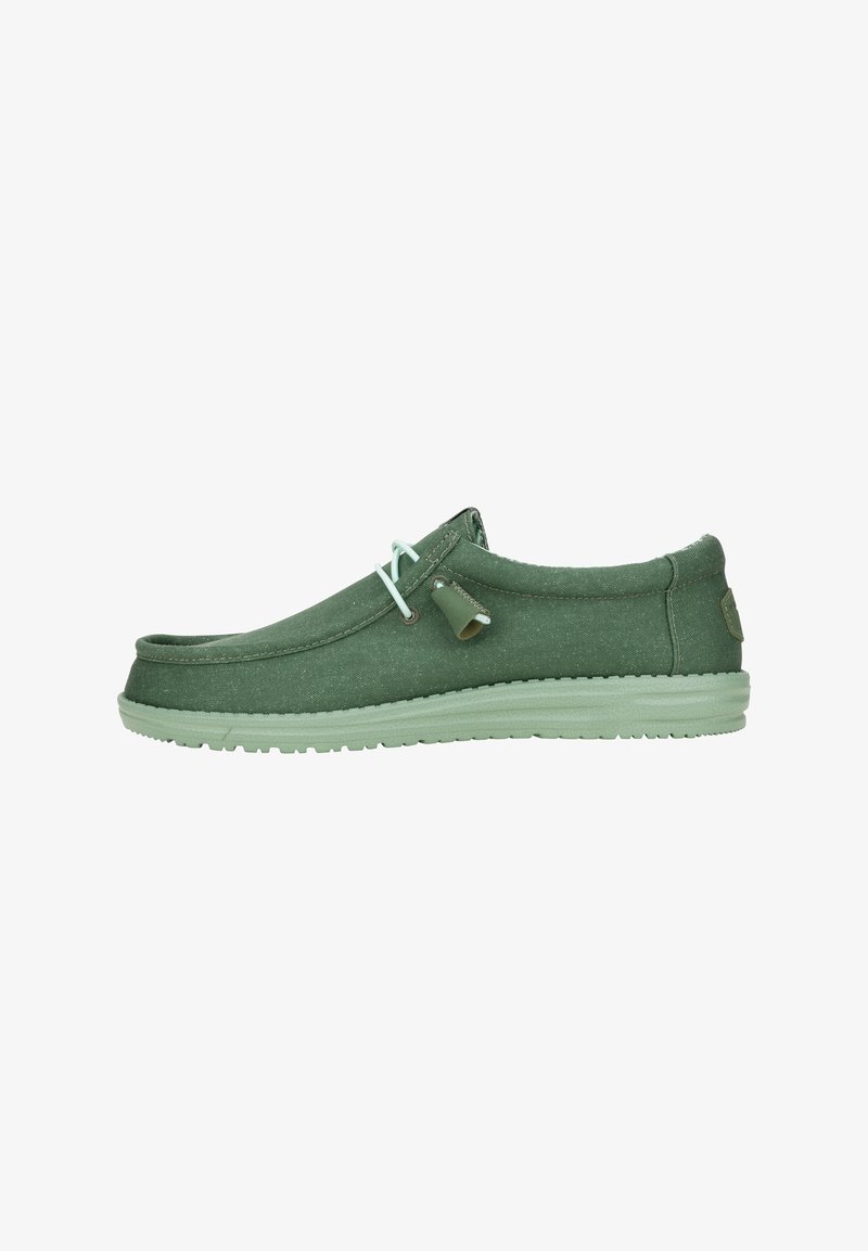Scarpa slip-on verde in tela con punta arrotondata, suola in gomma verde chiaro e lacci a contrasto. Texture liscia e dettagli di design semplici.