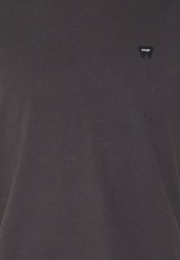 Tissu gris foncé avec un petit patch noir du logo Wrangler cousu près du côté supérieur gauche.