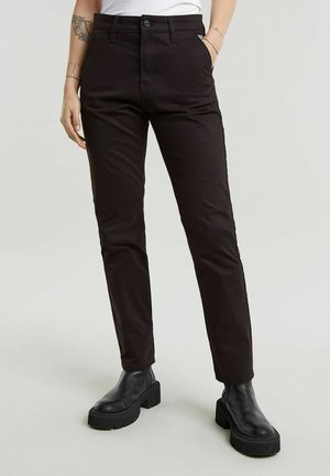 Pantaloni neri attillati, realizzati in un tessuto morbido con una leggera lucentezza. Presentano una chiusura con bottoni e tasche laterali, abbinati a stivali neri robusti.