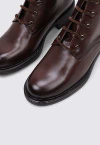 Brown leather ankle boots with a smooth finish, round toe, six eyelet lace-up design, and a contrasting dark sole.