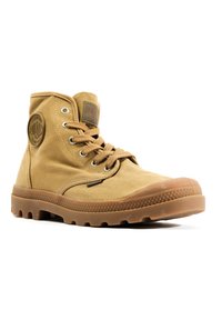 Bottine en toile beige avec semelle en caoutchouc, bout arrondi, œillets en métal et patch logo circulaire sur le côté extérieur.